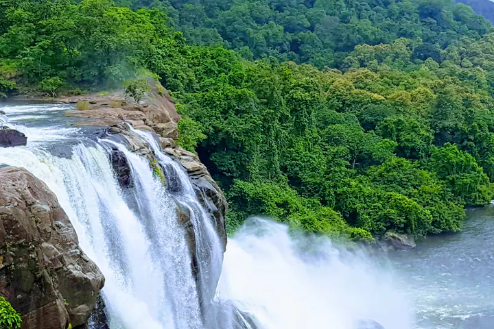 A wide view of Athirappilly waterfall and river through dense forest.